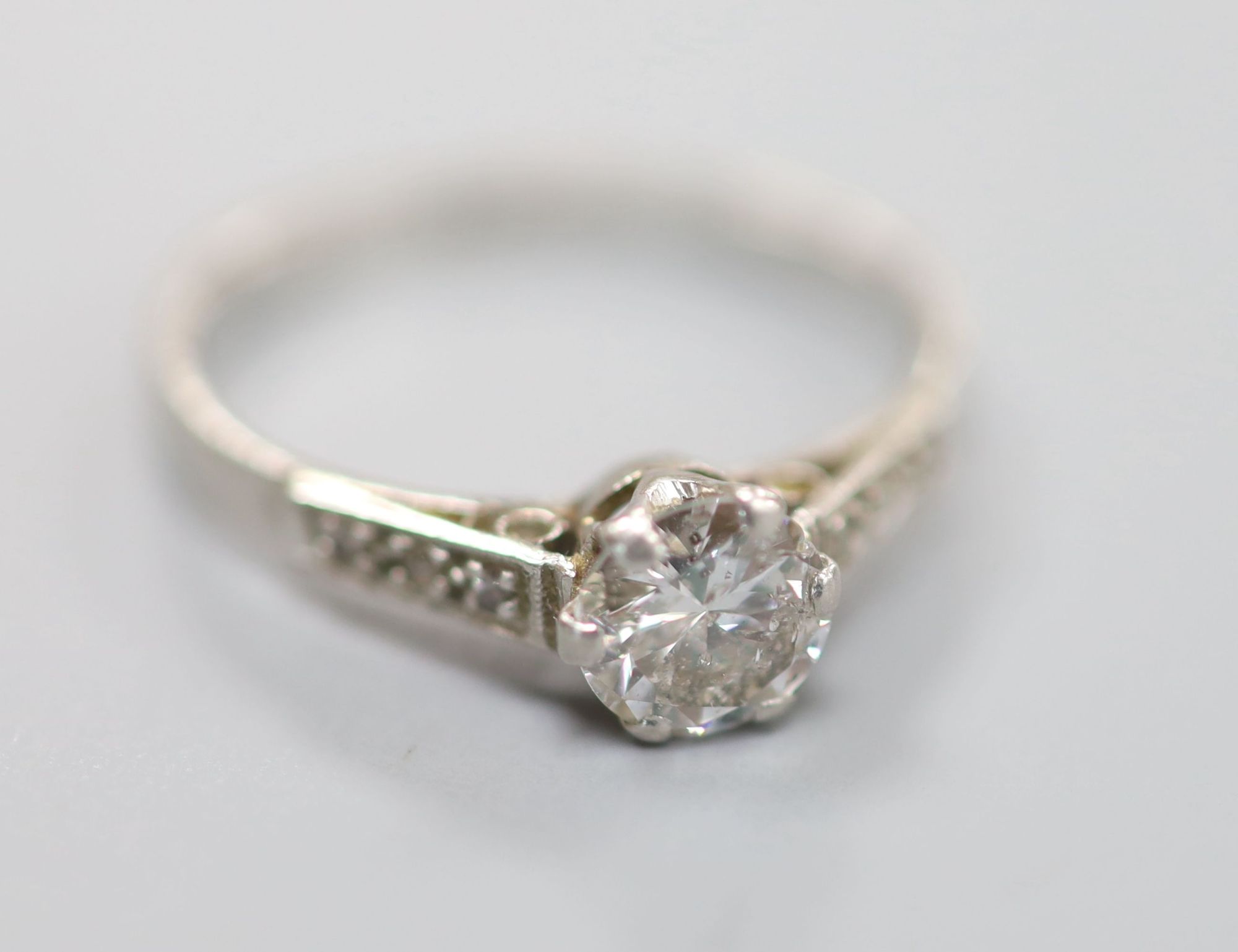 A white metal (stamped plat) platinum and single stone diamond ring, with diamond set shoulders, size M, gross 2.4 grams,